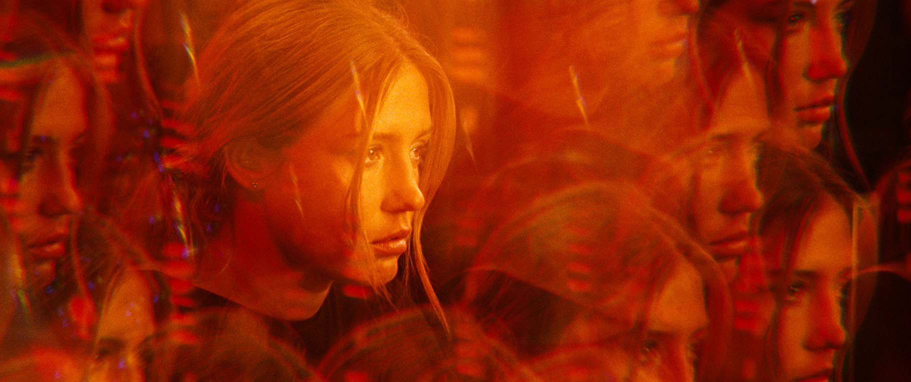 A still from The Five Devils. A woman's face is lit in red with a bunch of blurred copies of her face around her.