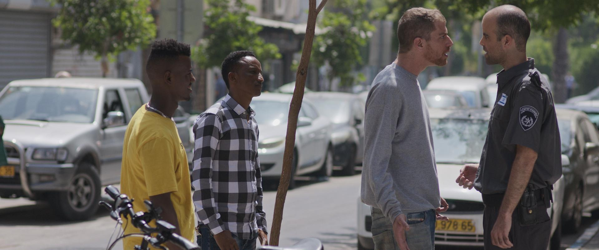 A still from Concerned Citizen. A white man is yelling at a cop while two black men stand behind him confused.