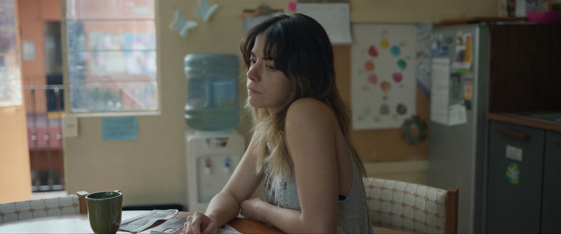 A still from All the Silence. Miriam is sitting in a breakroom and looking sad.
